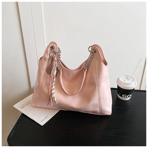Pink large tote bag with chain strap and tassel detail on a minimalist office desk