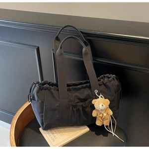 Detail of black canvas tote bag featuring a cute teddy bear pendant and drawstring closure