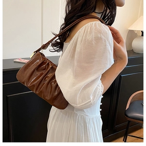 Brown ruched cloud bag in glossy leather shown on shoulder with minimalist style