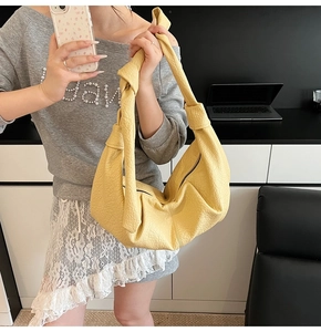 Close-up of yellow pleated crescent bag with knot detail and litchi grain leather
