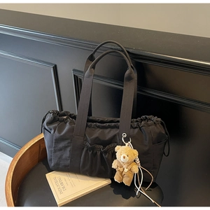 Detail of black canvas tote bag with drawstring closure and cute plush bear charm