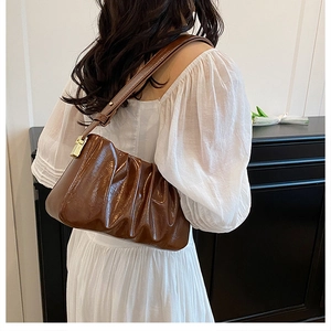 Brown ruched cloud bag with glossy leather and gold hardware detail on a model