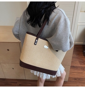 Close-up of woven straw tote bag featuring brown leather trim and metal logo plaque detail