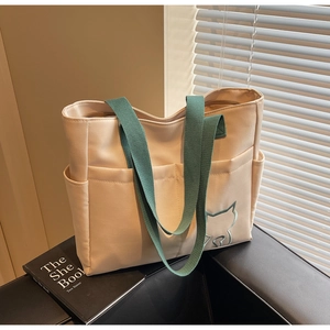 Close-up of canvas tote bag featuring cat embroidery, side pocket and green straps