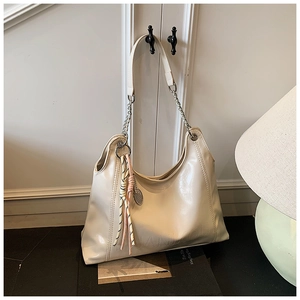 Detail of a large cream glossy tote bag with silver chain and woven rope charm