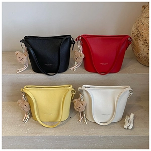 Detailed view of large bucket bags in four colors with cute plush bear charms on stone steps