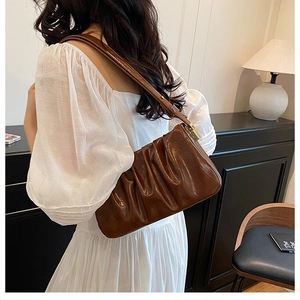 Brown ruched cloud bag with glossy finish shown on model wearing white pleated dress