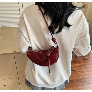 Detail of burgundy crescent leather crossbody bag showing rich texture and knot strap detail