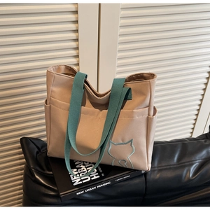 Detail of canvas tote bag with green handles and embroidered cat outline on a black sofa