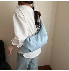 Detail of light blue crescent bag showing pleated leather texture and integrated strap