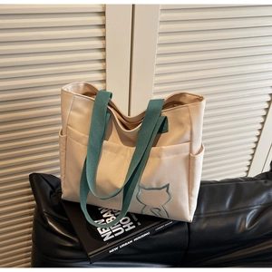 Detail view of canvas tote bag featuring multiple front pockets and green strap embroidery