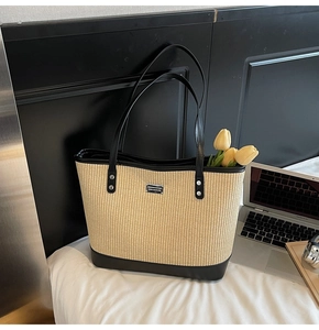 Detail of woven straw tote bag with black leather trim, laptop, and floral decor