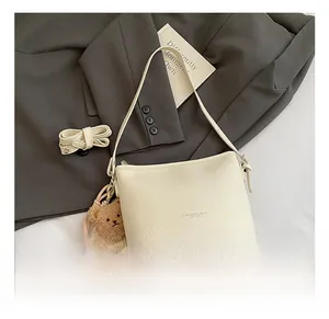 Detail of beige lychee texture bucket bag with cute brown bear charm and extra strap