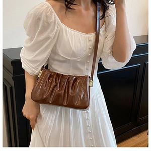 Detail of a dark brown pleated cloud bag on model showing rich leather texture and style