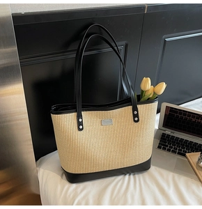 Detail of woven straw tote bag with black leather straps and silver metal logo plate