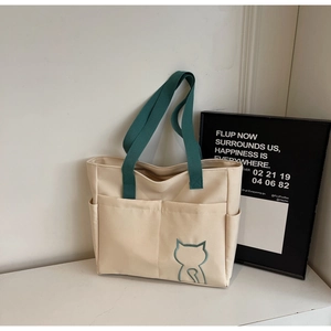 Detail of cream canvas tote bag with green handles and cute blue cat embroidery motif