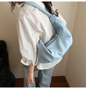 Lifestyle shot of light blue pebbled leather crossbody bag with knot shoulder strap detail