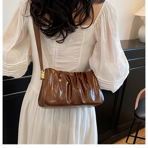 Detail of brown pleated cloud bag with glossy finish and gold metal buckle on the side