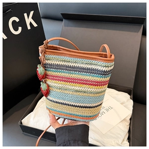 Détail du sac seau tissé à rayures colorées avec bandoulière en cuir et breloque fraise
