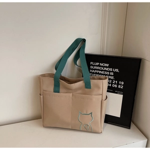 Detail of minimalist beige canvas tote bag featuring green handles and cat embroidery