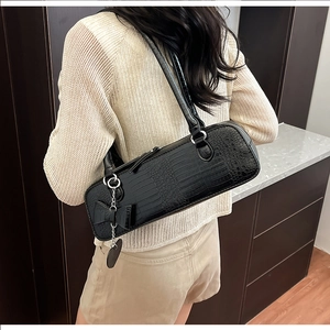 Détail du sac baguette noir texturé crocodile avec breloque cœur et nœud sur l'épaule