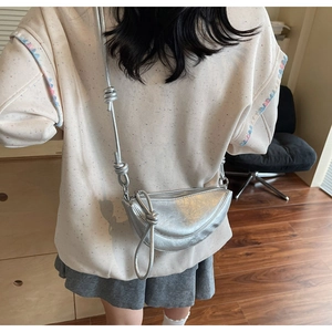 Detail of silver half-moon crossbody bag with decorative shoulder strap knots