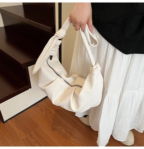 Detailed view of white pleated crescent bag with textured leather and knot strap design