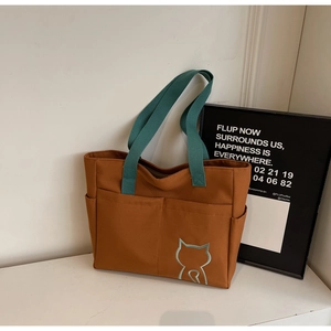 Detail of a brown canvas tote bag with green handles and minimalist cat embroidery