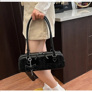 Détail du sac baguette noir texture croco avec breloques cœur et nœud sur la bandoulière