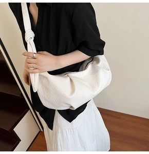Detail of white pleated croissant bag with premium litchi grain texture and knot strap