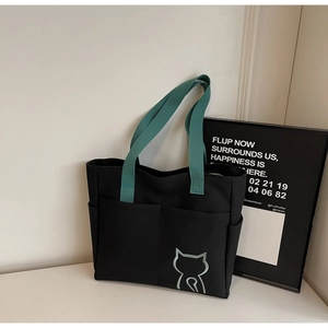 Detail of black canvas tote bag with green cat embroidery and double front pockets