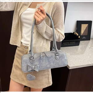 Détail d'un sac à main bleu avec relief crocodile, nœud et breloques en cœur