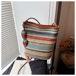Détail d'un sac seau tissé coloré avec des breloques fraises et une fine bandoulière brune