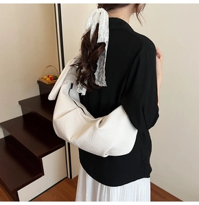 Detail view of white crescent bag with knotted shoulder strap and textured leather finish