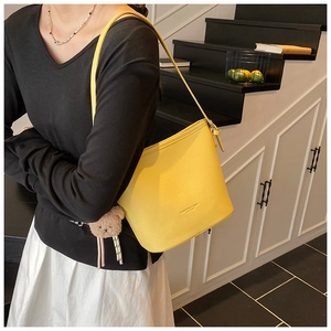 Detail of yellow lychee pattern bucket bag with brown teddy bear charm on a model