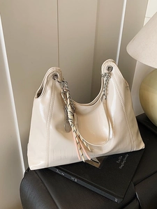 Chic beige glossy leather tote bag with silver chain handles and woven charm on a black case