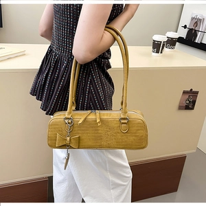 Détail du sac à bandoulière jaune moutarde à texture croco avec breloque nœud sur modèle
