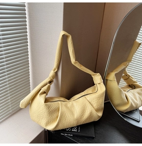 Close-up of light yellow crescent bag featuring pleated texture and unique knotted strap
