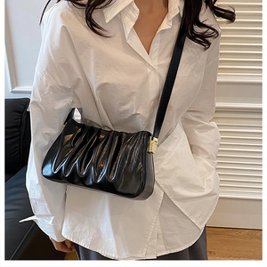 Detail of black pleated cloud shoulder bag featuring glossy leather and gold hardware