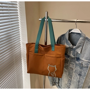 Detail of canvas tote bag with green handles and embroidered cat silhouette on front pocket