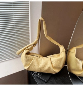 Detail view of yellow pleated crescent bag featuring stylish knotted shoulder strap texture