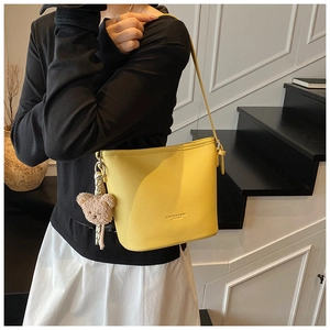 Detail of yellow bucket bag with lychee grain leather texture and cute bear pendant