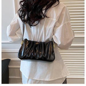 Detail of black pleated cloud bag with glossy finish and gold metal buckle on model