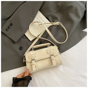 Detail of cream white glossy leather handbag featuring embossed bow and silver buckles