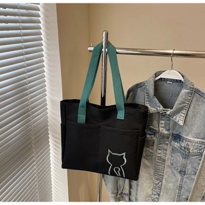 Detail of black canvas tote bag with blue cat embroidery and green fabric handles