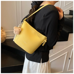 Yellow bucket bag with lychee texture and plush bear charm shown on a model