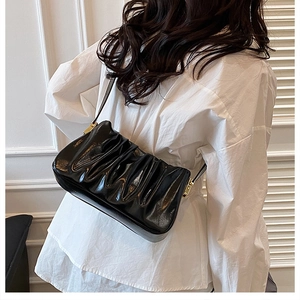 Detail of black pleated cloud bag featuring glossy leather and golden metal buckle