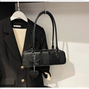 Détail du sac à bandoulière en similicuir croco noir avec nœud et pendentif cœur
