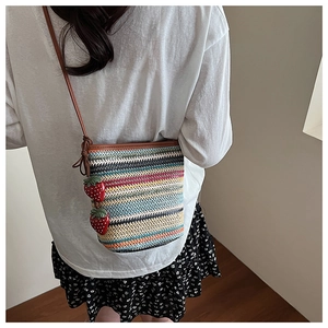 Détail d'un sac bandoulière tissé arc-en-ciel avec breloques fraises et lanières brunes