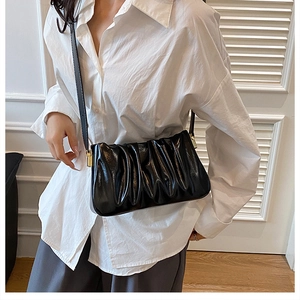 Detailed view of black pleated cloud bag with shiny texture and golden metal hardware